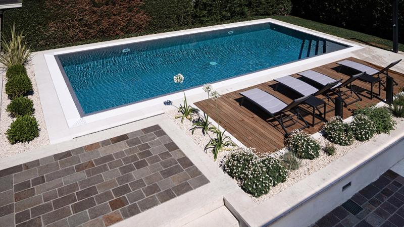 Piscina privata con deck in legno, aiuole fiorite e pavimentazione in pietra